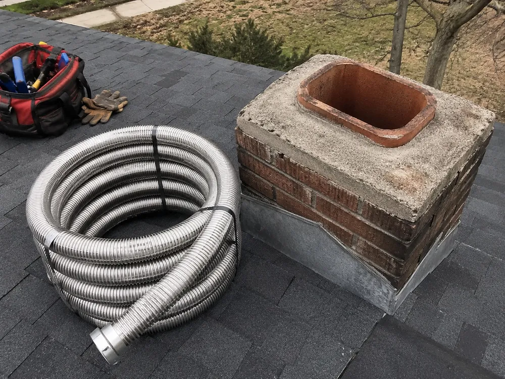 A coil of stainless steel chimney liner on a roof beside an open clay flue
